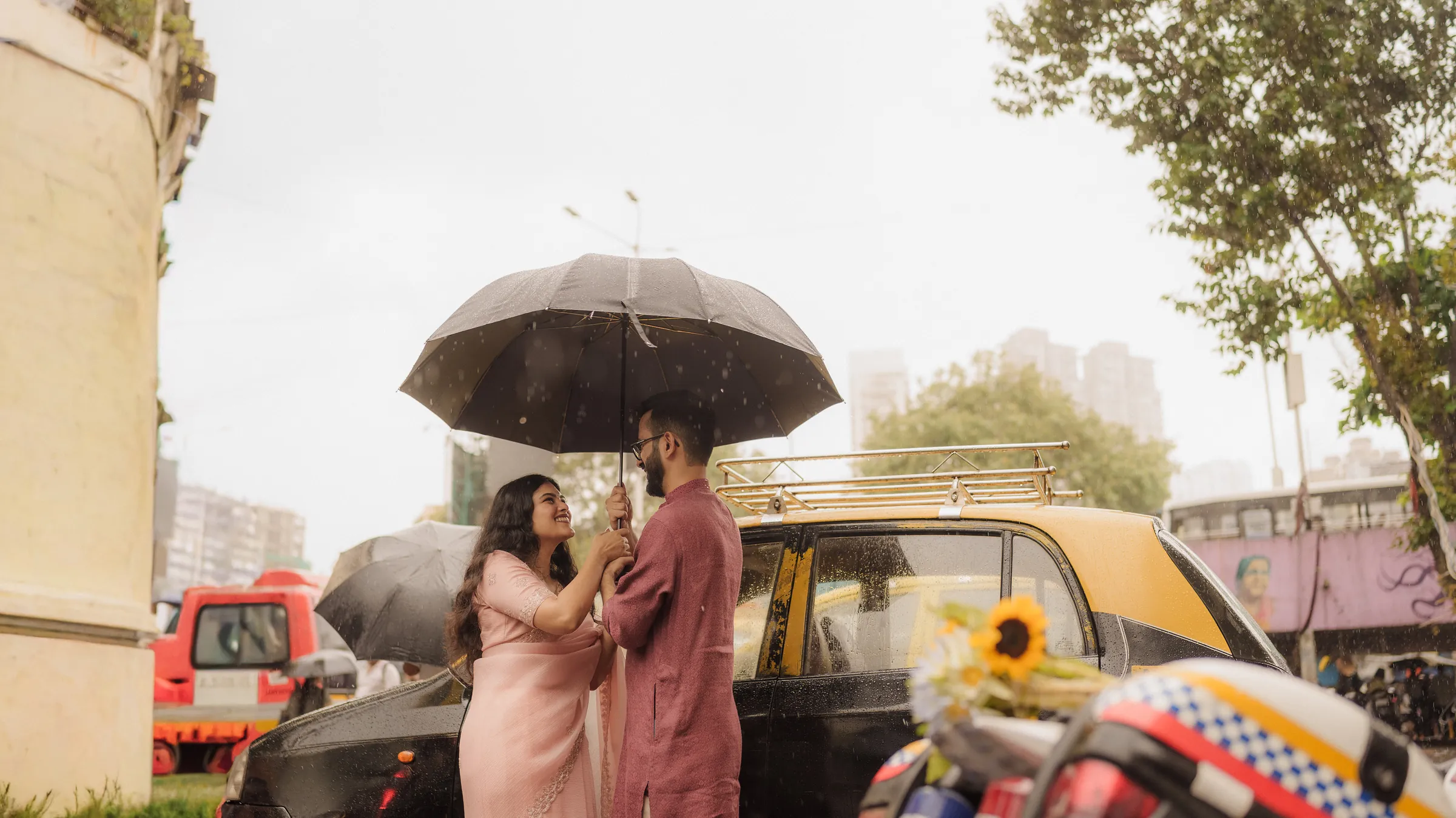 Yash and Manasi under one umbrella beside a black-and-yellow taxi in the Mumbai rain